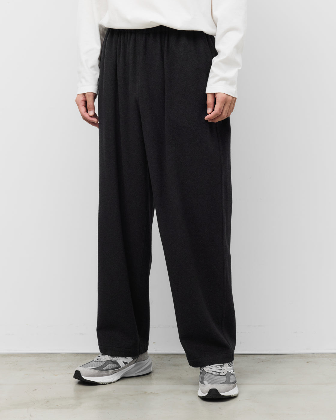 白い長袖TシャツとholkのKang Fu Pants（チャコール）を合わせたリラックススタイル。イージーウエストのワイドシルエット、裾元のクッション、SUPER160sラムウールのドレープ。足元はグレーのスニーカー。Relaxed Wide Pants & Sneakers