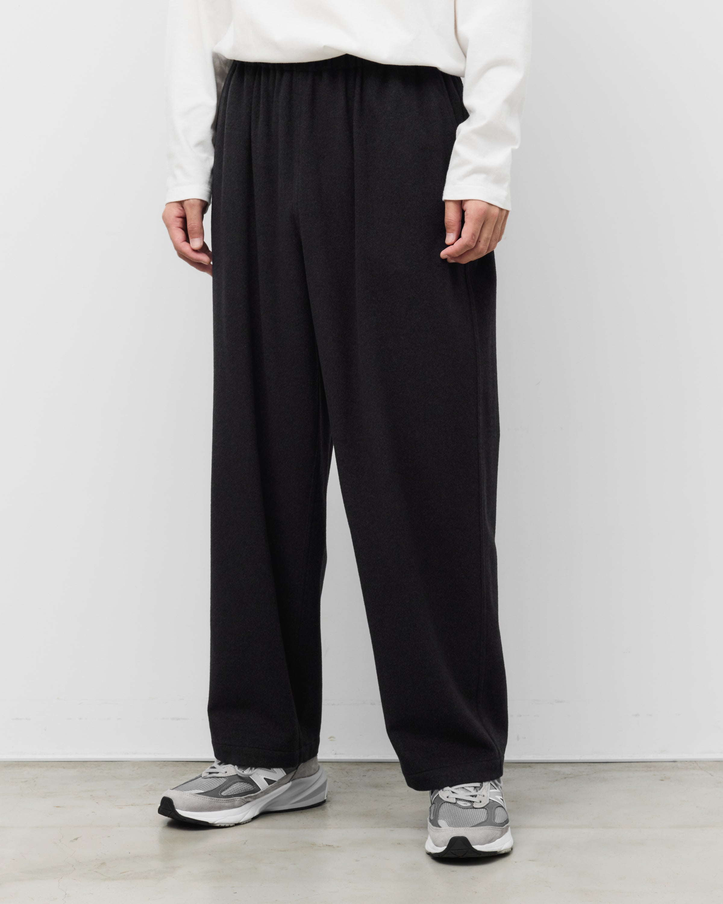 白い長袖TシャツとholkのKang Fu Pants（チャコール）を合わせたリラックススタイル。イージーウエストのワイドシルエット、裾元のクッション、SUPER160sラムウールのドレープ。足元はグレーのスニーカー。Relaxed Wide Pants & Sneakers
