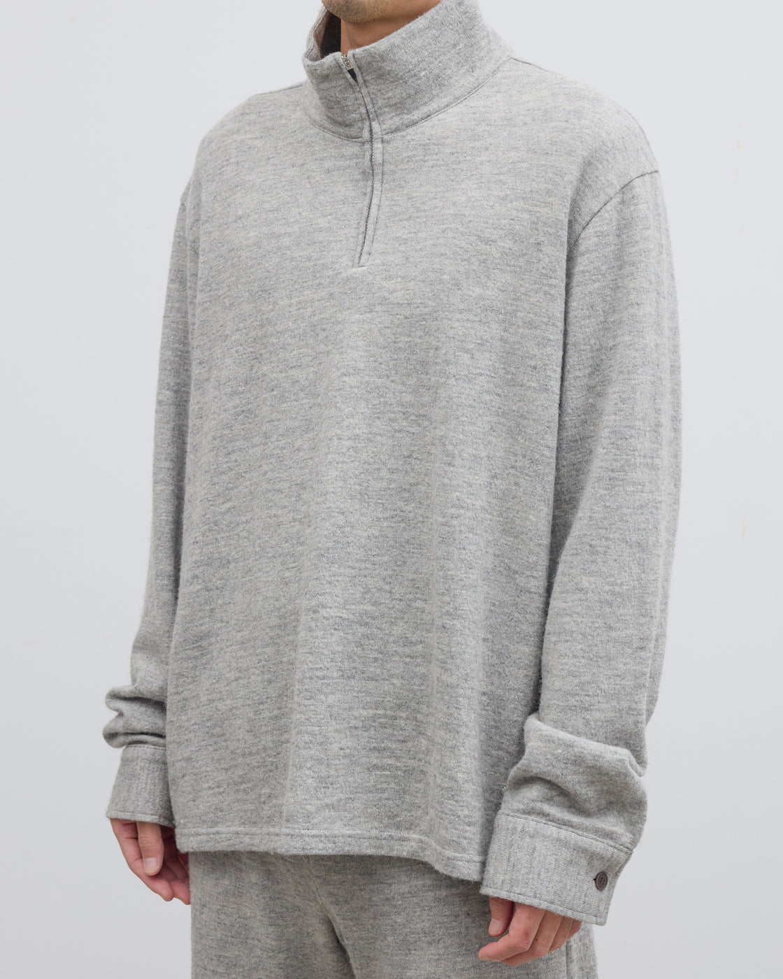 グレーのハーフジップニットプルオーバーを着用したモデルの横顔、シェットランドウールとコットンの混紡素材による柔らかな肌当たりとスウェットのようなリラックス感のある表情が魅力
