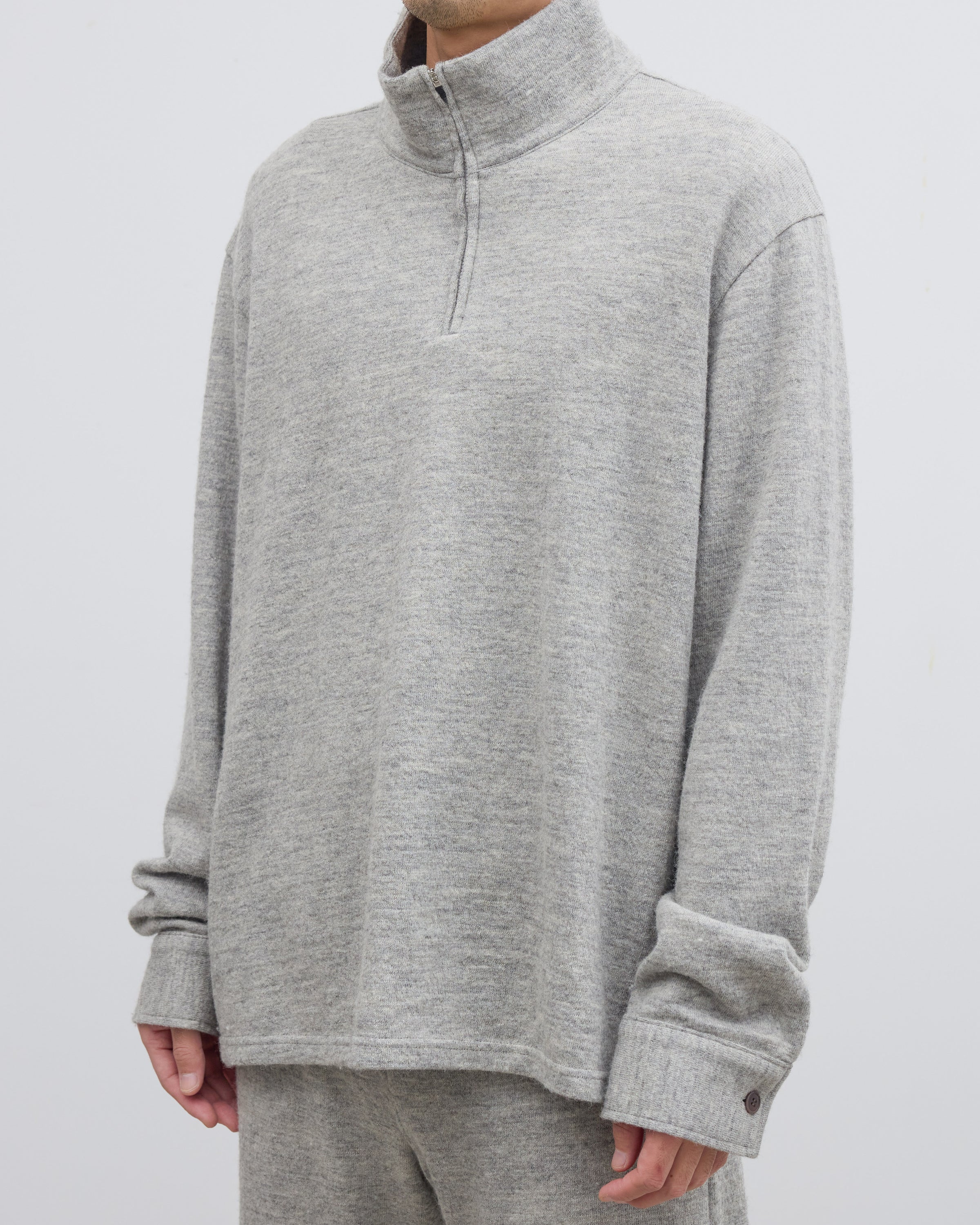 グレーのハーフジップニットプルオーバーを着用したモデルの横顔、シェットランドウールとコットンの混紡素材による柔らかな肌当たりとスウェットのようなリラックス感のある表情が魅力