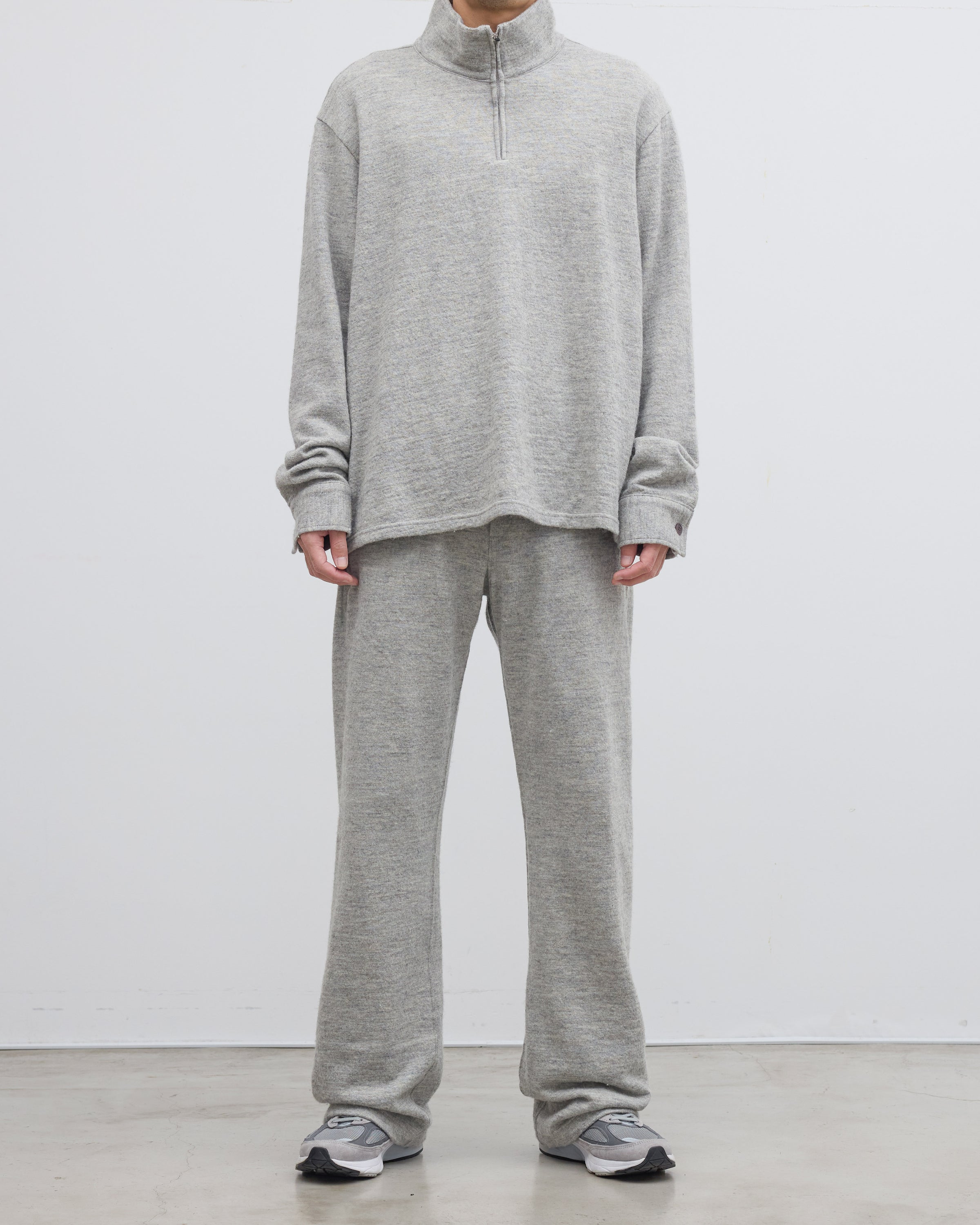グレーのメランジ糸ハーフジップニットプルオーバーを着用したモデルの後ろ姿、シェットランドウールとコットンの撚り合わせによる独特な風合いと尾州産ニットの高い品質が感じられる一枚